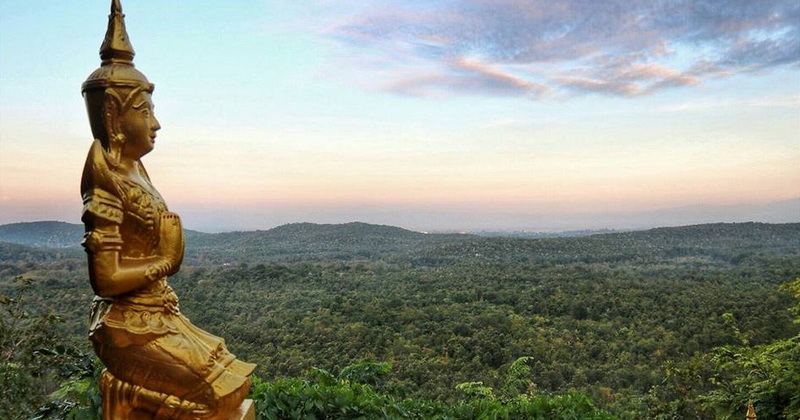 Thai Statue with Scenic Hills at Phra That in Kwaen Golden Thai statue overlooking green hills and a partly cloudy sky at Phra That in Kwaen.