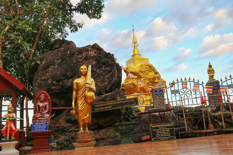 Golden Stupa and Religious Statues at Wat Phra That in Kwaen Golden stupa with statues and flags surrounded by rocks under blue sky at Wat Phra That in Kwaen.