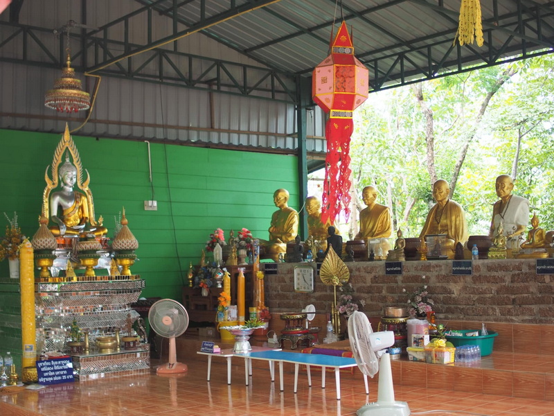 Indoor shrine featuring a large Buddha statue and six monk statues with offerings and decorations at Phra That in Kwaen.