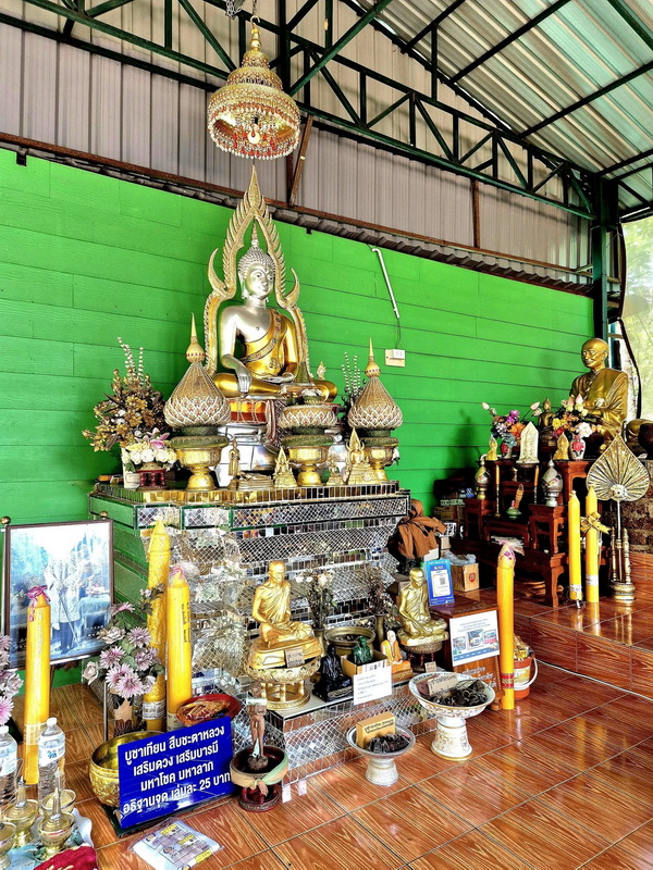 Inside the Shrine with Buddha Statues at Phra That in Kwaen Inside shrine with Buddha statues, flowers, candles, and vibrant green wall at Phra That in Kwaen.