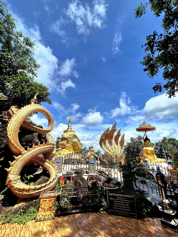 Serpent Sculptures and Buddha at Kwaen at Phra That in Kwaen Golden serpent sculptures and a Buddha statue on a platform with a chedi in the background at Phra That in Kwaen.
