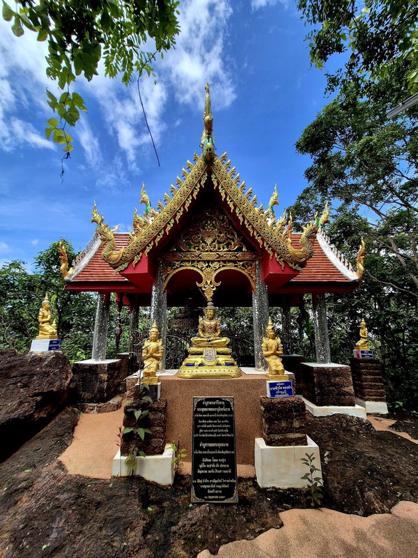 Outdoor Shrine with Gold Statues at Phra That in Kwaen Small ornate shrine with gold statues and decorated roof surrounded by trees and sky at Phra That in Kwaen.