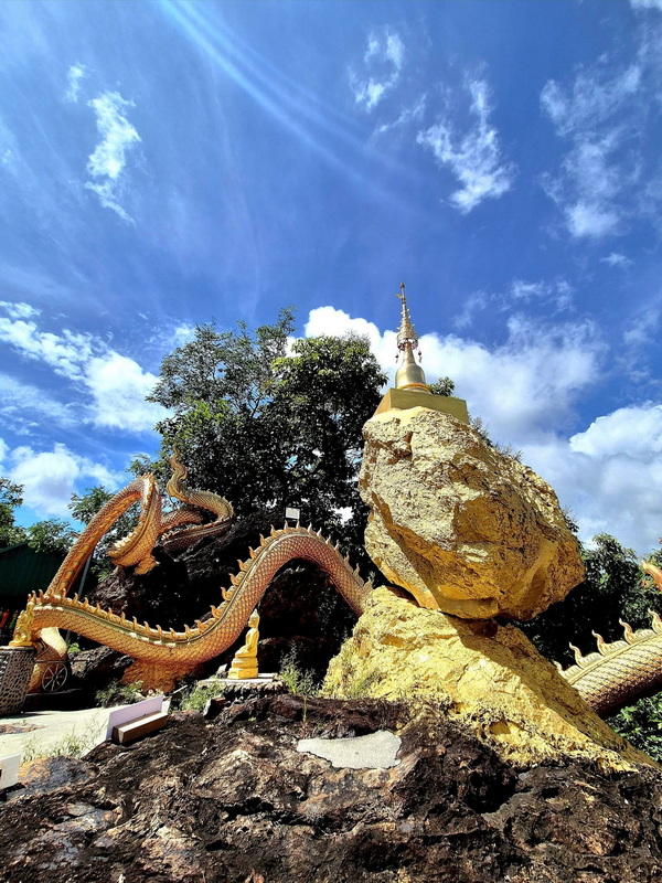 Golden stupa on a rock with serpent statue under bright blue sky at Phra That in Kwaen.