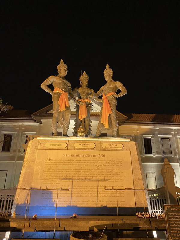 Three illuminated guardian statues standing on a monument at night with a building in the background at Three kings Monument.