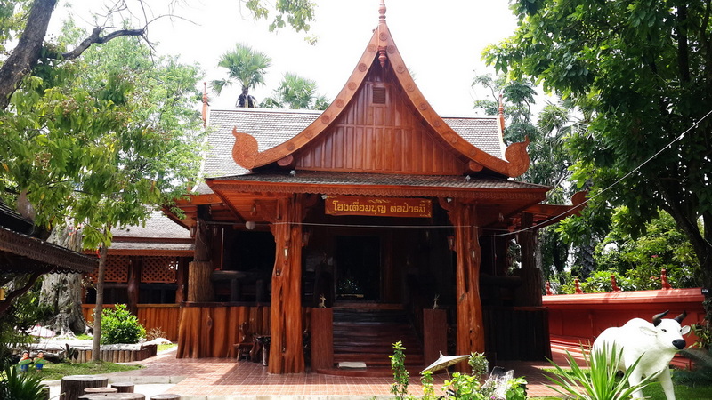 Traditional Wooden Temple at Wat Chamadevi Wooden temple with curved roof, green trees, and plants surrounding it at Wat Chamadevi.