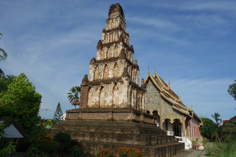 Ancient brick pagoda with multiple tiers in a lush garden setting at Wat Chamadevi.