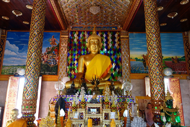 Inside a temple with a large golden Buddha statue surrounded by colorful murals and ornate pillars at Wat Chamadevi.