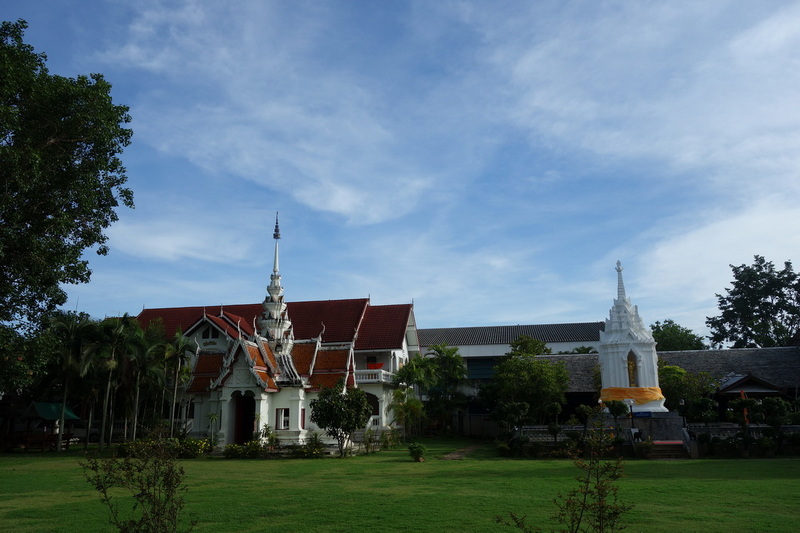 White temple with spires, red roofs, and surrounding greenery under a partly cloudy sky at Wat Chamadevi.