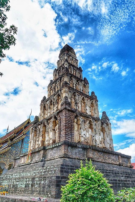 Ancient Stone Pagoda at Wat Chamadevi Tall stone pagoda with carved details under a blue sky and clouds at Wat Chamadevi.