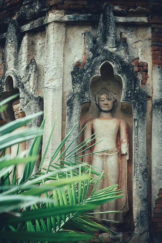 Ancient Buddha Statue at Wat Chamadevi Ancient Buddha sculpture in an arched niche amidst weathered wall and green plants at Wat Chamadevi.