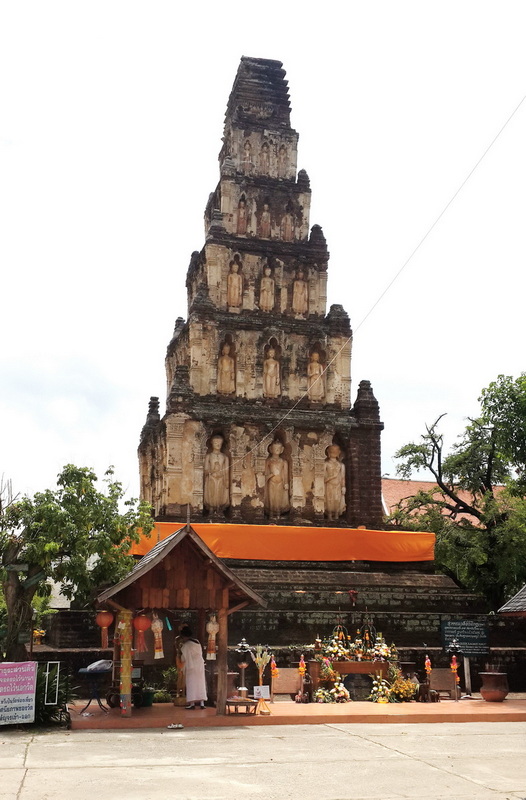 Ancient brick stupa with Buddha statues and offerings at the base, surrounded by trees at Wat Chamadevi.
