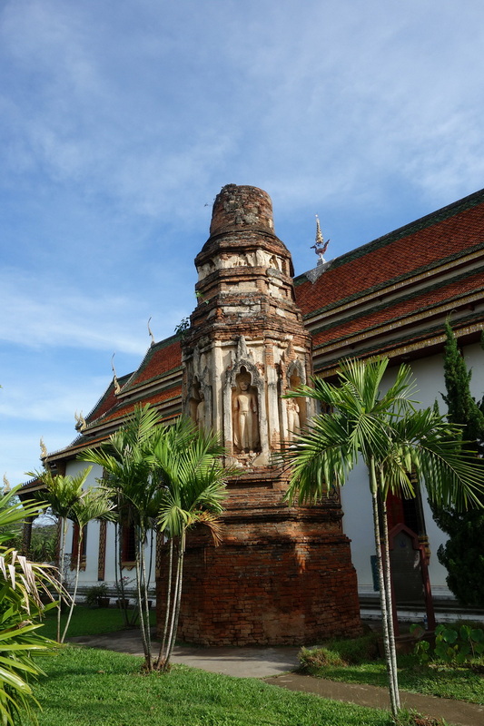 Brick stupa with Buddha niche and surrounding palm trees near temple building at Wat Chamadevi.