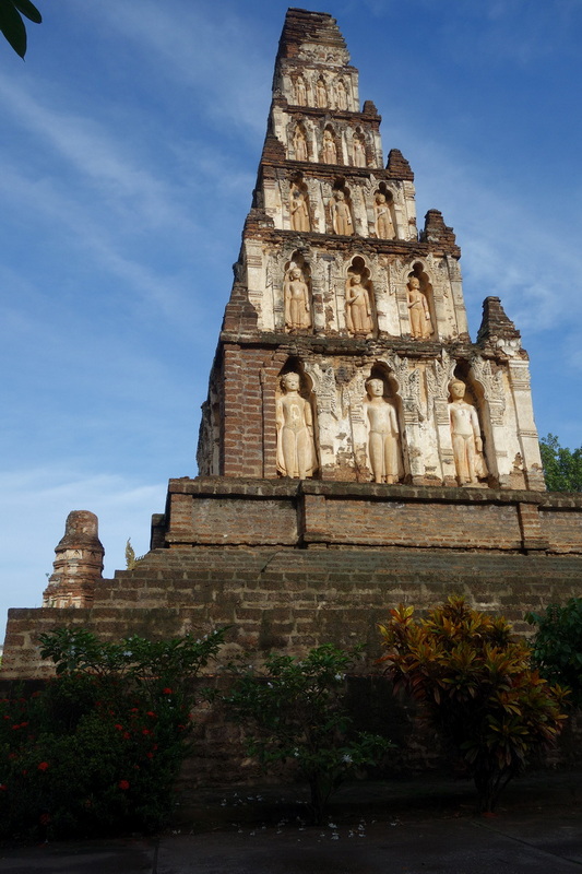 Ancient brick stupa with multiple tiers and Buddha statues against a blue sky at Wat Chamadevi.