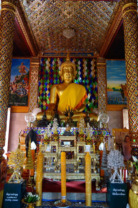 Golden Buddha statue inside a colorful temple with intricate patterns and smaller statues at Wat Chamadevi.