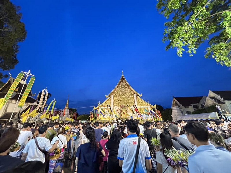 Traditional Thai Temple Gathering at Wat Chedi Luang Crowd gathered at a decorated Thai temple with banners under a clear evening sky at Wat Chedi Luang.