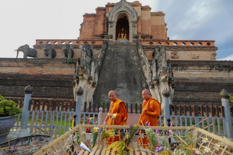 Two monks in orange robes gather near an old brick temple with sculptures of elephants at Chedi Luang temple.
