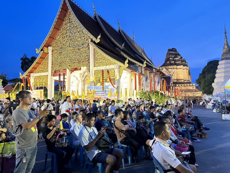 People seated in front of a golden temple with a stupa at dusk in Chiang Mai at Wat Chedi Luang.