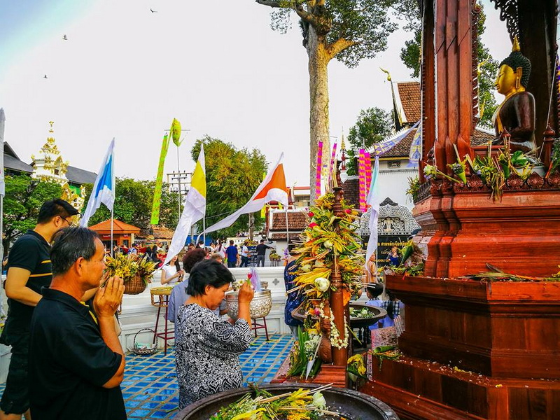 Praying at a Buddhist Shrine at Wat Chedi Luang People praying and making offerings at a Buddhist shrine with flags and trees nearby at Wat Chedi Luang.