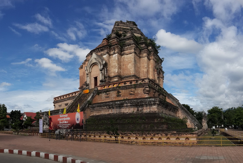 Ancient stone temple with stairs and tiered roof against blue sky at Chedi Luang temple.