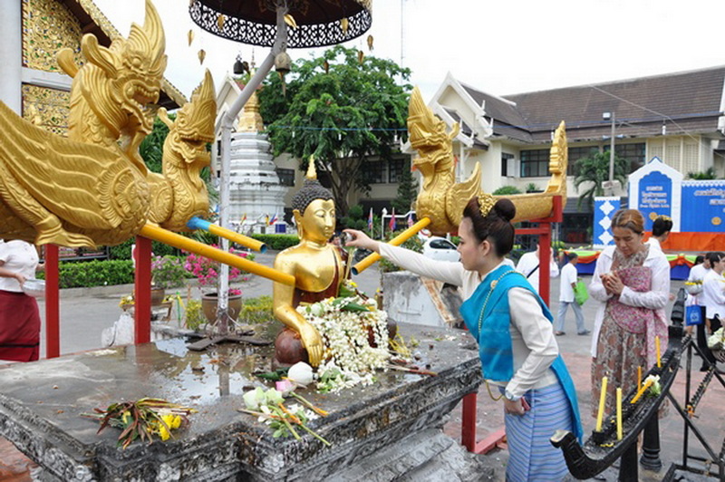 Woman making offering at a golden Buddha statue with decorative dragon sculptures and flower garlands at Wat Chedi Luang.