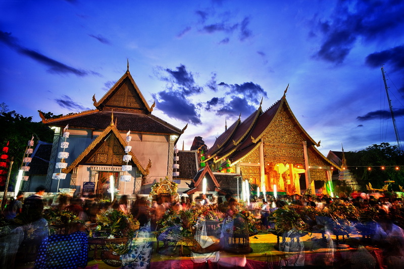 Night view of illuminated Thai temples with crowds and festive lights at Wat Chedi Luang.