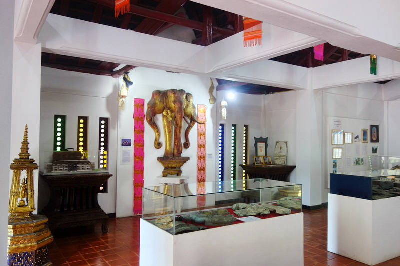 Indoor exhibit featuring a golden elephant statue and display cases with artifacts at Chedi Luang temple.