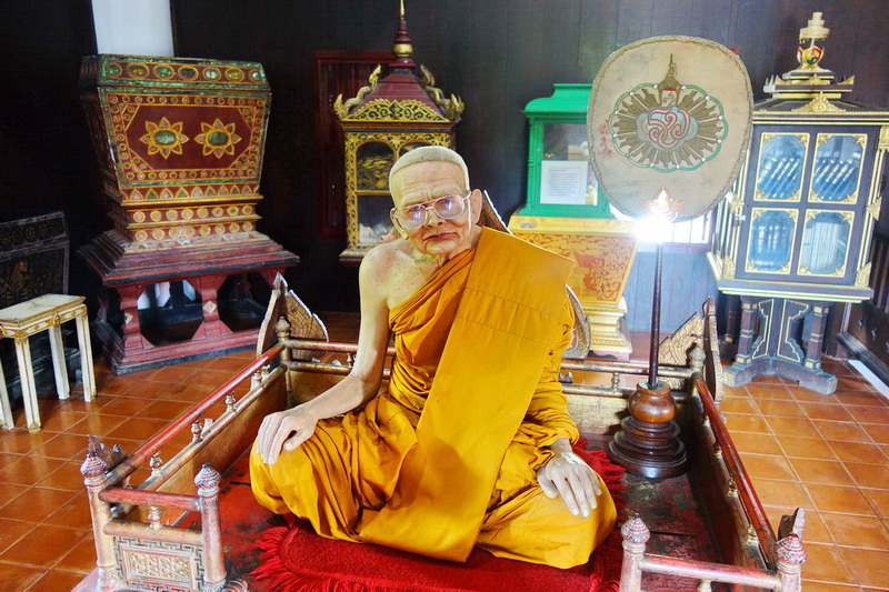 Buddhist Monk Statue Inside Temple at Wat Chedi Luang Statue of a monk in orange robes seated inside a decorated temple room at Wat Chedi Luang.