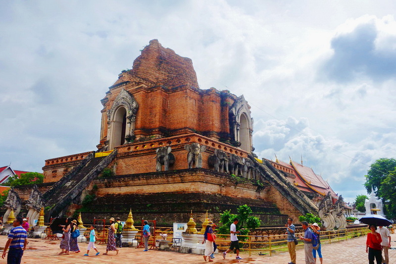 Ancient Brick Stupa at Wat Chedi Luang Ancient brick stupa with carved details and visitors in courtyard under cloudy sky at Wat Chedi Luang.
