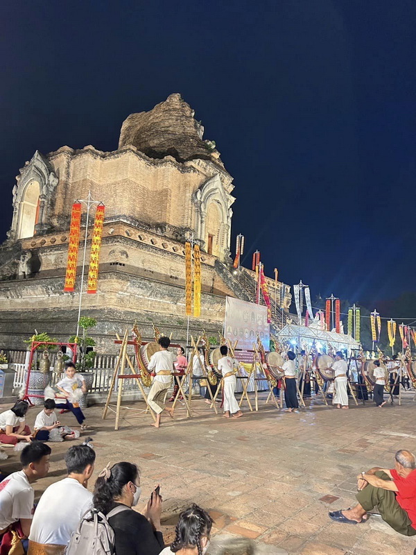 Night scene with performers in front of an ancient temple with banners hanging nearby at Chedi Luang temple.