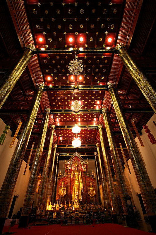 Inside a temple with gold pillars, chandeliers, and a central Buddha statue at Chedi Luang temple.