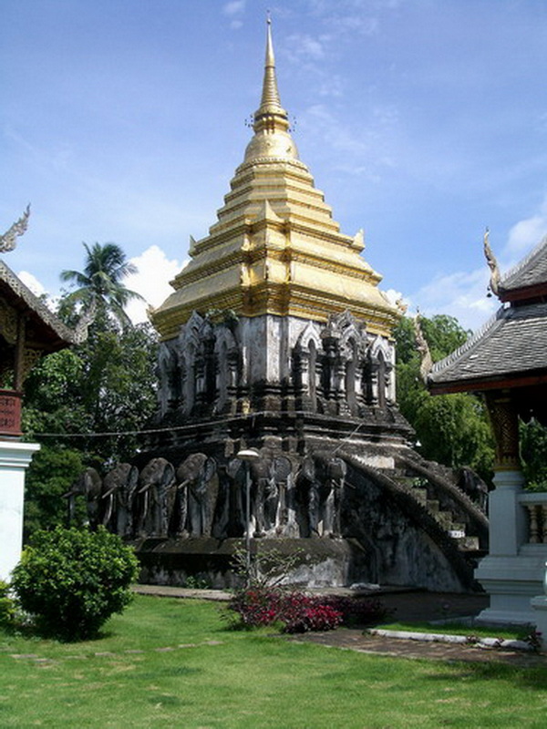 Temple Stupa with Gold and Silver Details at Chiang Man Temple Tall temple stupa with gold and silver details, surrounded by trees and traditional buildings at Chiang Man Temple.