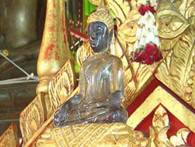 Dark wooden sculpture of a seated figure with gold leaf backdrop and intricate details at Wat Chiang Man.