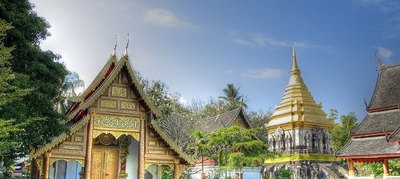 Traditional Thai temple with golden stupa and decorative roofs shown outdoors at Chiang Man Temple.