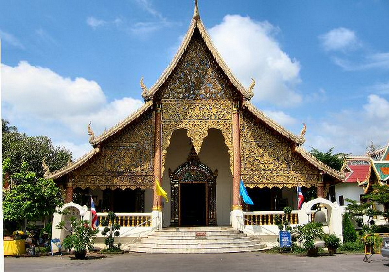 Ornate Thai temple entrance with gold details and flags outside at Chiang Man Temple.
