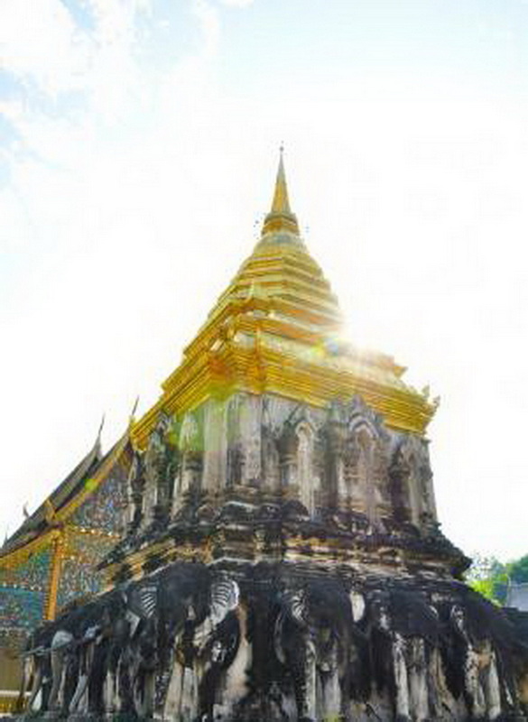 Golden Temple and Elephant Statues at Wat Chiang Man Golden stupa with elephant statues beneath, bright sunlight shining behind at Wat Chiang Man.