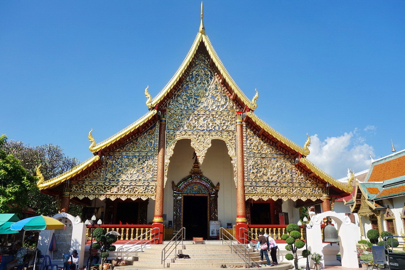 Beautifully decorated temple with intricate gold details and a multi-tiered roof under a blue sky at Wat Chiang Man.