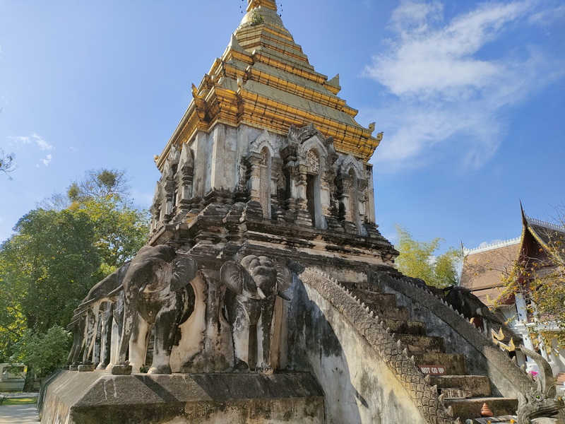 Golden stupa with elephant statues and carvings under a partly cloudy sky at Wat Chiang Man.