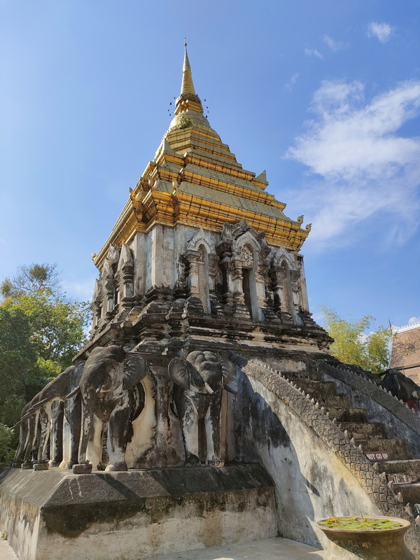 Golden Pagoda with Carvings at Wat Chiang Man Tall golden pagoda with detailed carvings and stairs leading up, under a clear blue sky at Wat Chiang Man.