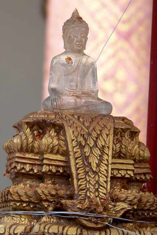 Metal Buddha statue sitting on a richly carved wooden pedestal with detailed leaf carvings at Chiang Man Temple.