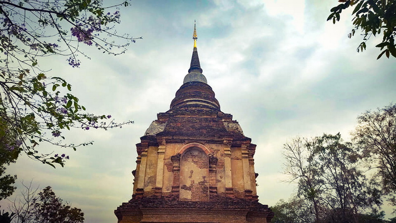 Ancient Temple Stupa at Wat Jed Yod Ancient temple stupa with pointed spire surrounded by trees and cloudy sky at Wat Jed Yod.