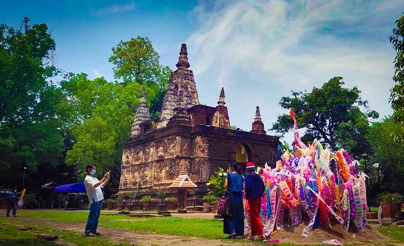 Ancient Temple Scene at Wat Jed Yod Ancient brick temple with multiple spires surrounded by trees and visitors at Wat Jed Yod.