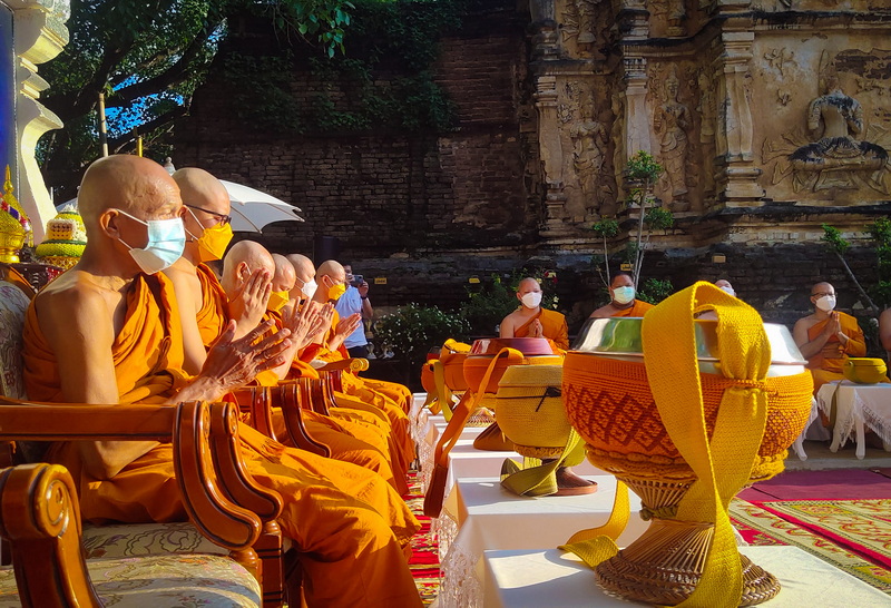 Monks wearing robes and masks participating in a prayer ceremony outdoors at Wat Jed Yod.