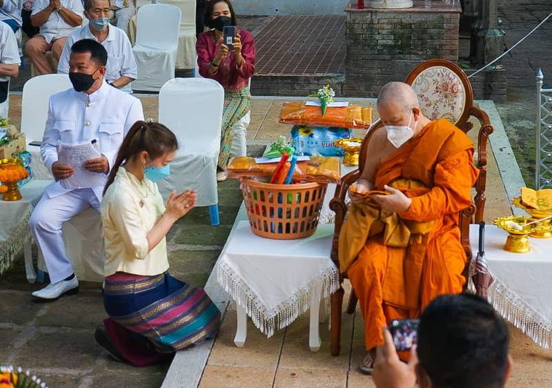 Woman praying before monk seated on ornate chair during a religious ceremony at Wat Jed Yod.