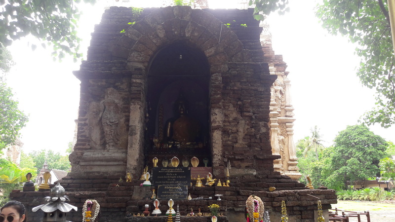 Ancient Brick Shrine with Buddha at Wat Jed Yod Brick shrine with seated Buddha statue surrounded by offerings and greenery at Wat Jed Yod.