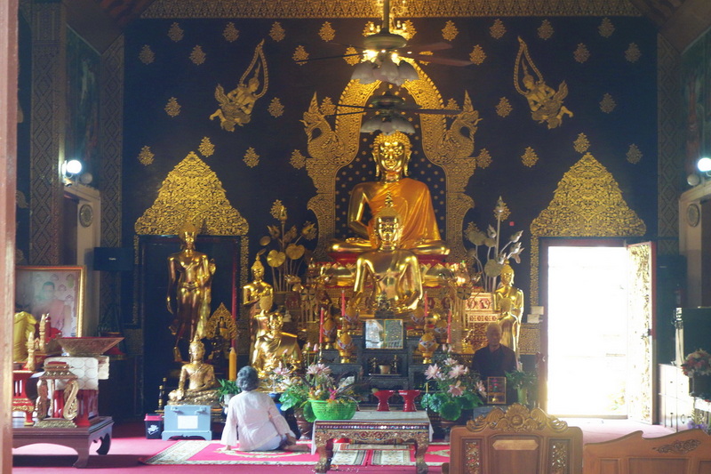 Temple Interior with Buddha Statue at Wat Jed Yod Woman sitting before a large golden Buddha statue inside ornate temple at Wat Jed Yod.