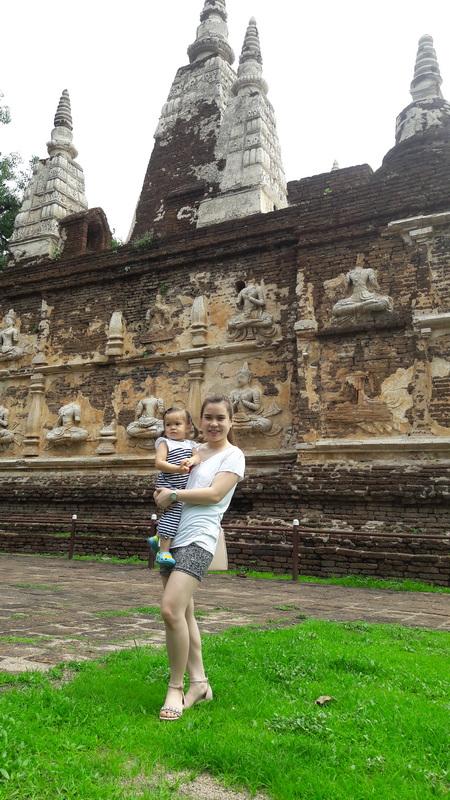 Ancient Temple Wall with Statues at Wat Jed Yod Woman holding child in front of ancient brick temple wall with statues and stupas at Wat Jed Yod.