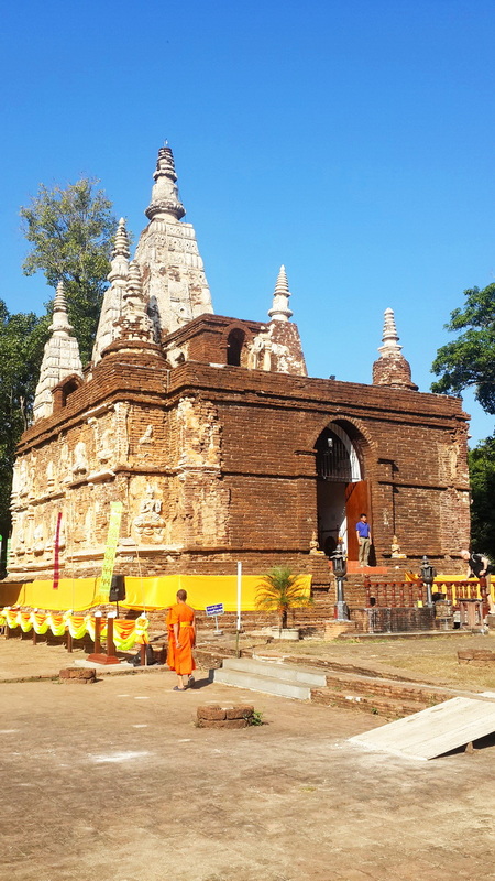 Ancient brick pagoda with spires under a clear blue sky, visitors nearby at Wat Jed Yod.