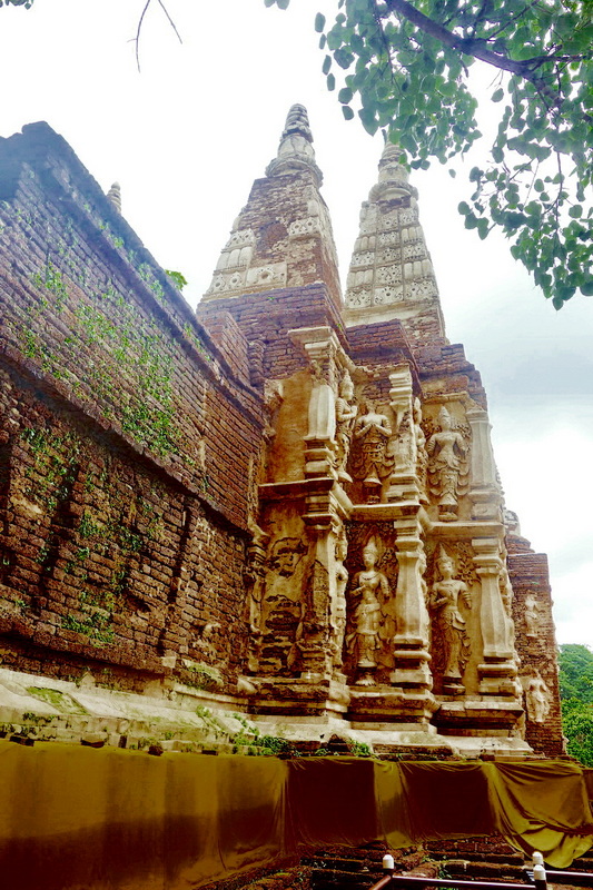 Ancient temple with sculptures and tall spires surrounded by greenery at Wat Jed Yod.