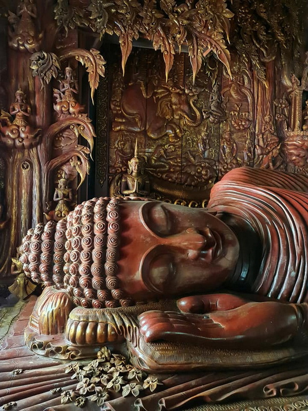 Large wooden reclining Buddha statue with carved details and floral adornments at Wat Luang Khun Win.