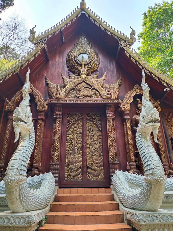 Decorative Temple Entrance at Wat Luang Khun Win Wooden temple entrance with detailed carvings and mythical serpent statues on each side of steps at Wat Luang Khun Win.